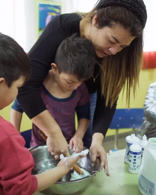Una voluntaria acompaña a dos chicos en un taller.